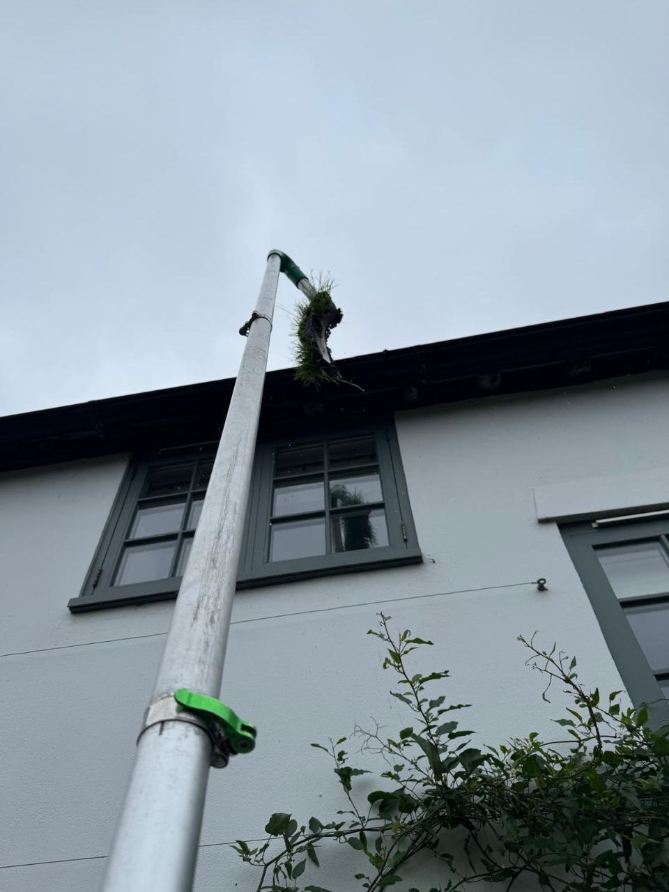 Vacuuming moss and debris from the gutter of a tall house with a reach pole in West Sussex